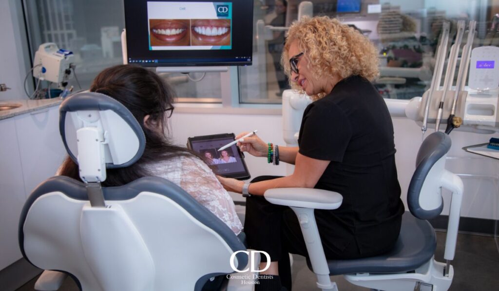 Dentist with a tablet showing smile photos while consulting a patient in a modern dental chair room.