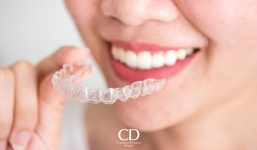 Close-up of a person holding a clear dental aligner near their teeth with a smile in the background.